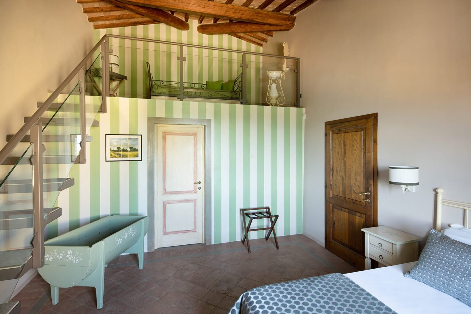 Charming interior of a two-level bedroom featuring green and white striped walls, a spiral staircase, a cozy bed with patterned linens, and rustic wooden accents. The space showcases a blend of modern and traditional design elements, creating a welcoming atmosphere. | Only on SopranoVillas