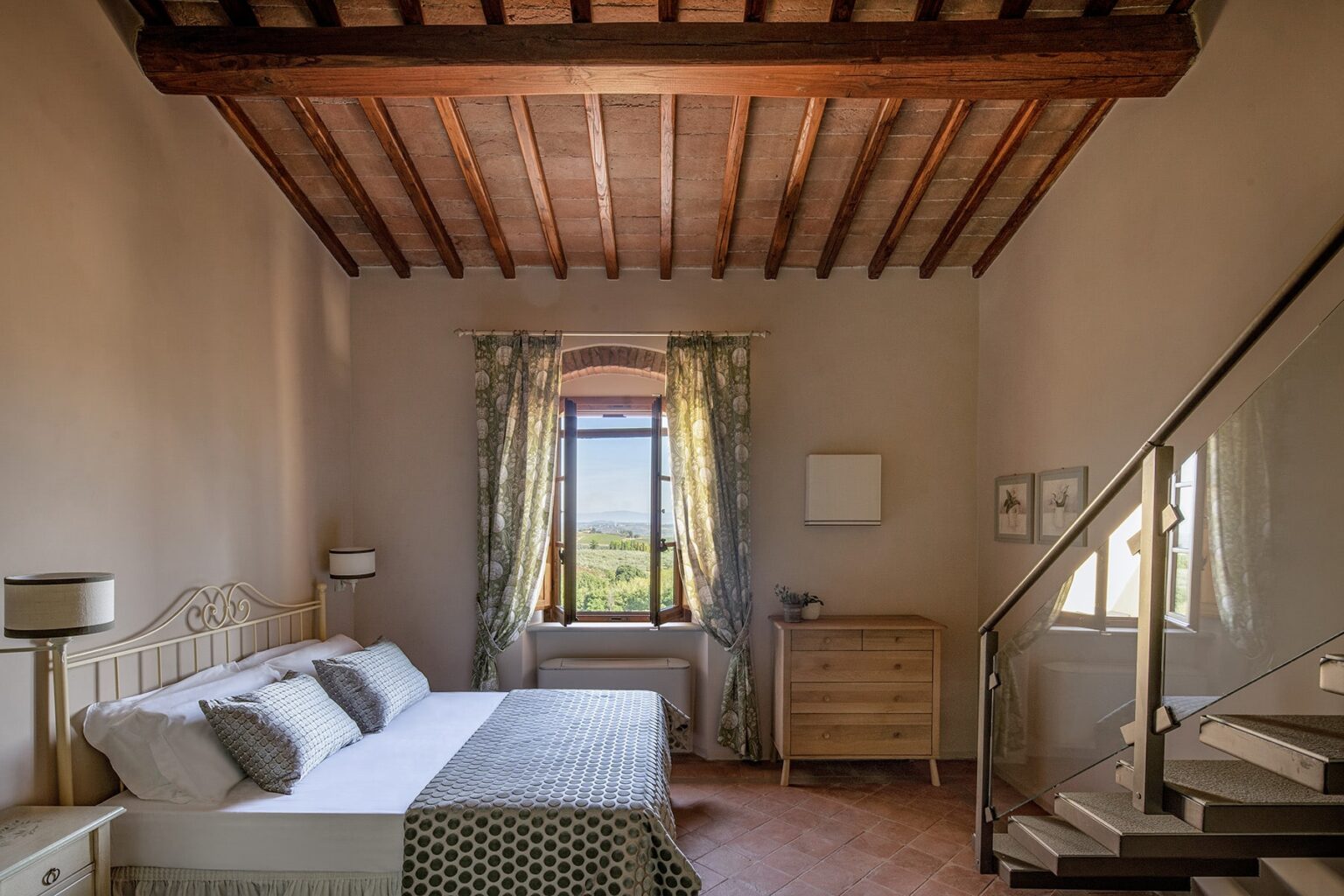 Cozy bedroom interior featuring a wooden beam ceiling, a large window with scenic views, a comfortable bed with decorative pillows, and a stylish dresser. The room combines modern furnishings with rustic charm, creating a serene atmosphere. | Only on SopranoVillas