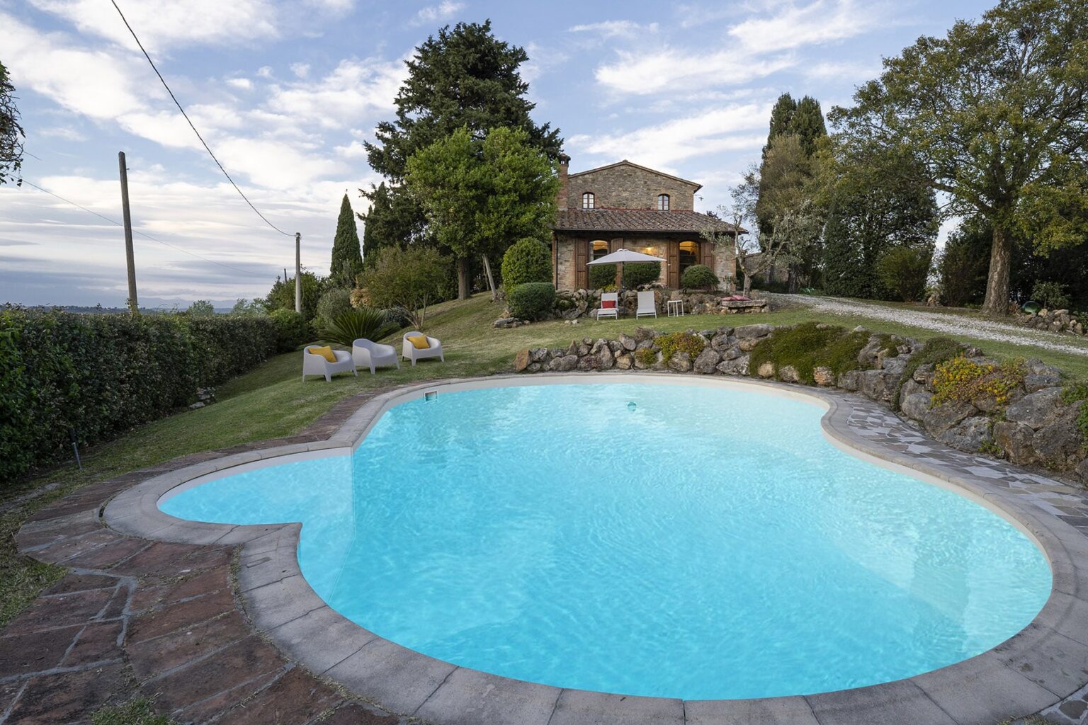 Inviting outdoor pool with a unique heart shape, surrounded by lush greenery and a rustic stone house in the background, ideal for relaxation and leisure. | Only on SopranoVillas