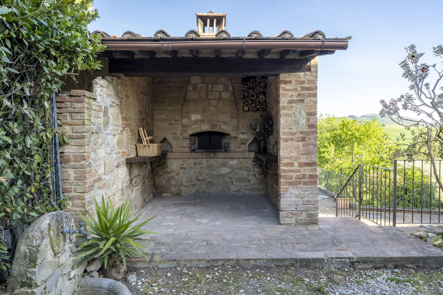 Rustic outdoor kitchen with a stone oven, surrounded by greenery and a paved patio, offering a serene view of the landscape. | Only on SopranoVillas