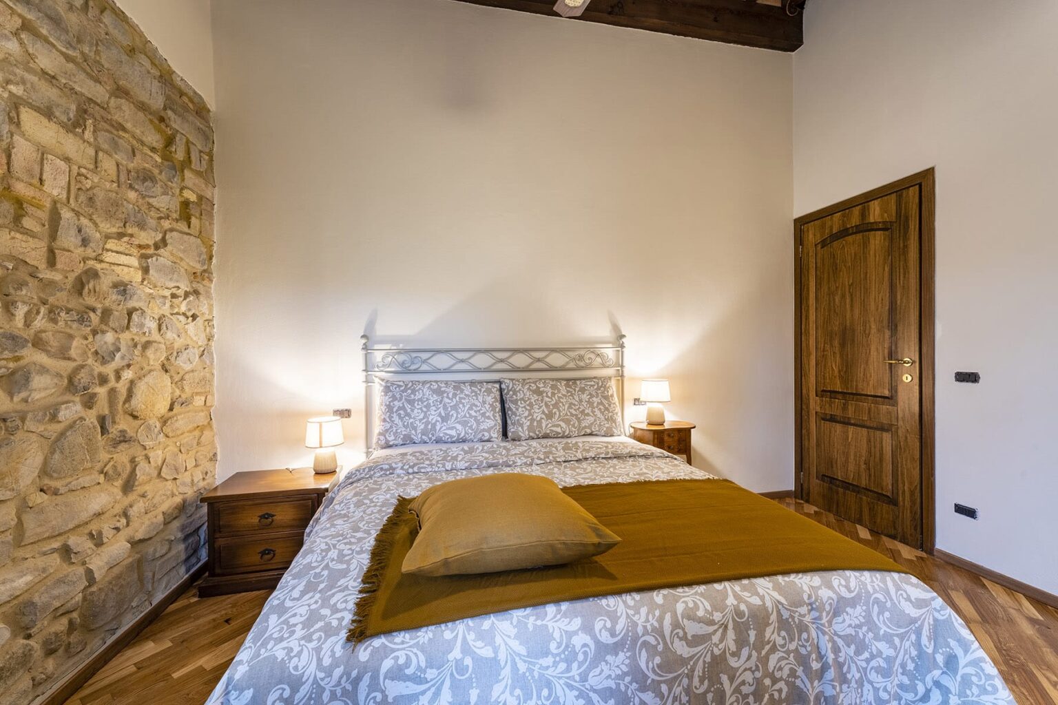 Cozy bedroom featuring a decorative bed with a patterned duvet, wooden furniture, and a rustic stone wall, creating a warm and inviting atmosphere. | Only on SopranoVillas
