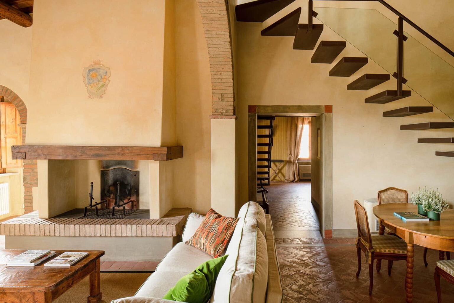 Cozy living room interior featuring a white sofa, wooden dining table, and a staircase, with a rustic fireplace and warm, inviting decor. | Only on SopranoVillas