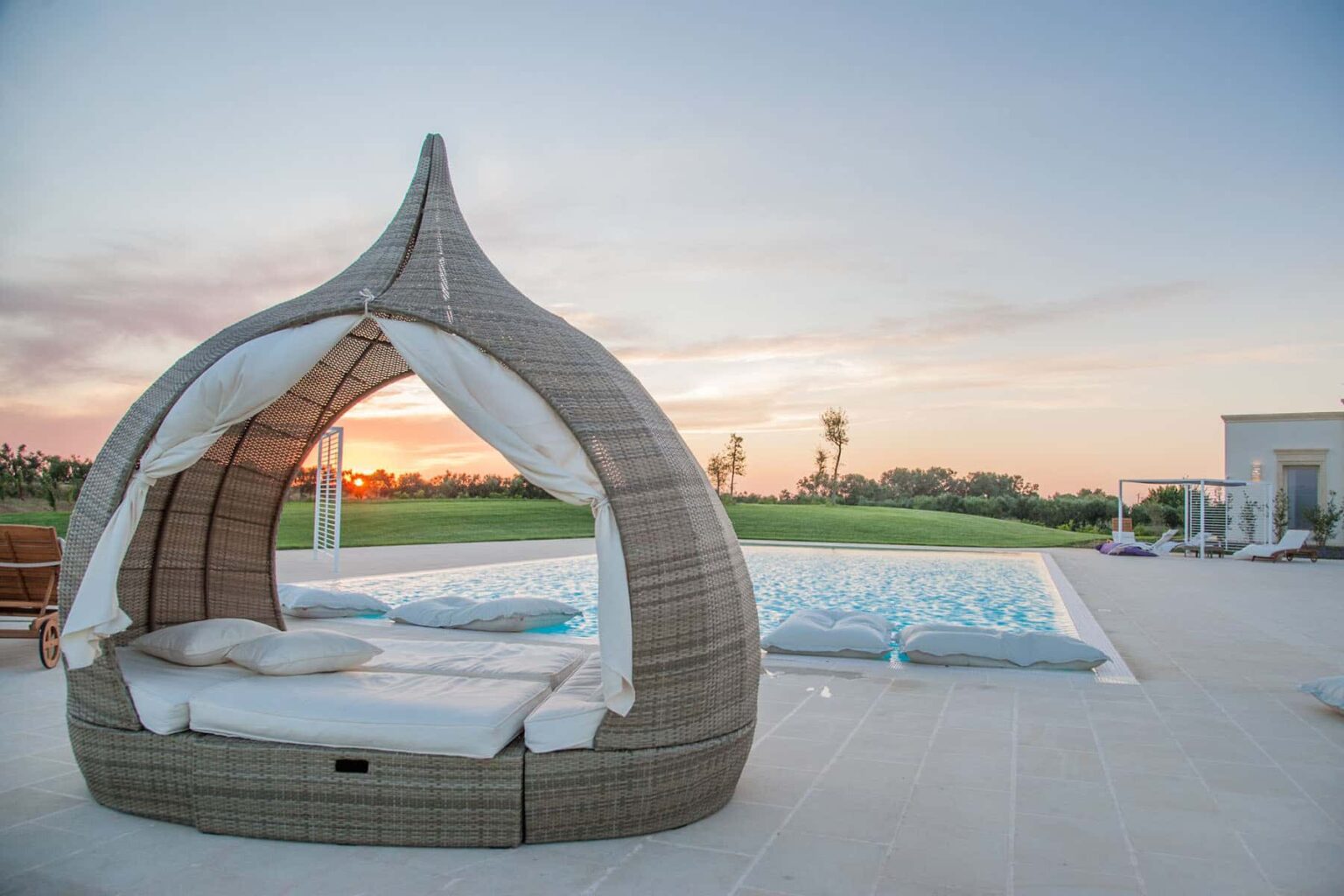 Cozy outdoor daybed near a swimming pool at sunset, featuring a unique woven design and plush cushions, set in a serene landscape. | Only on SopranoVillas