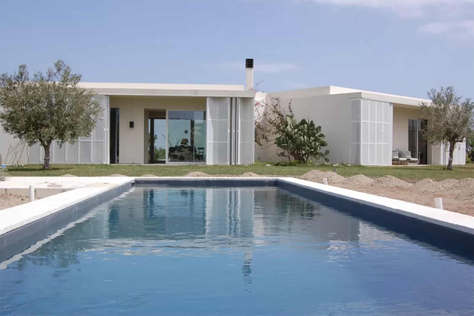 Modern villa with a sleek design, featuring large glass windows and a tranquil swimming pool surrounded by landscaped gardens. | Only on SopranoVillas