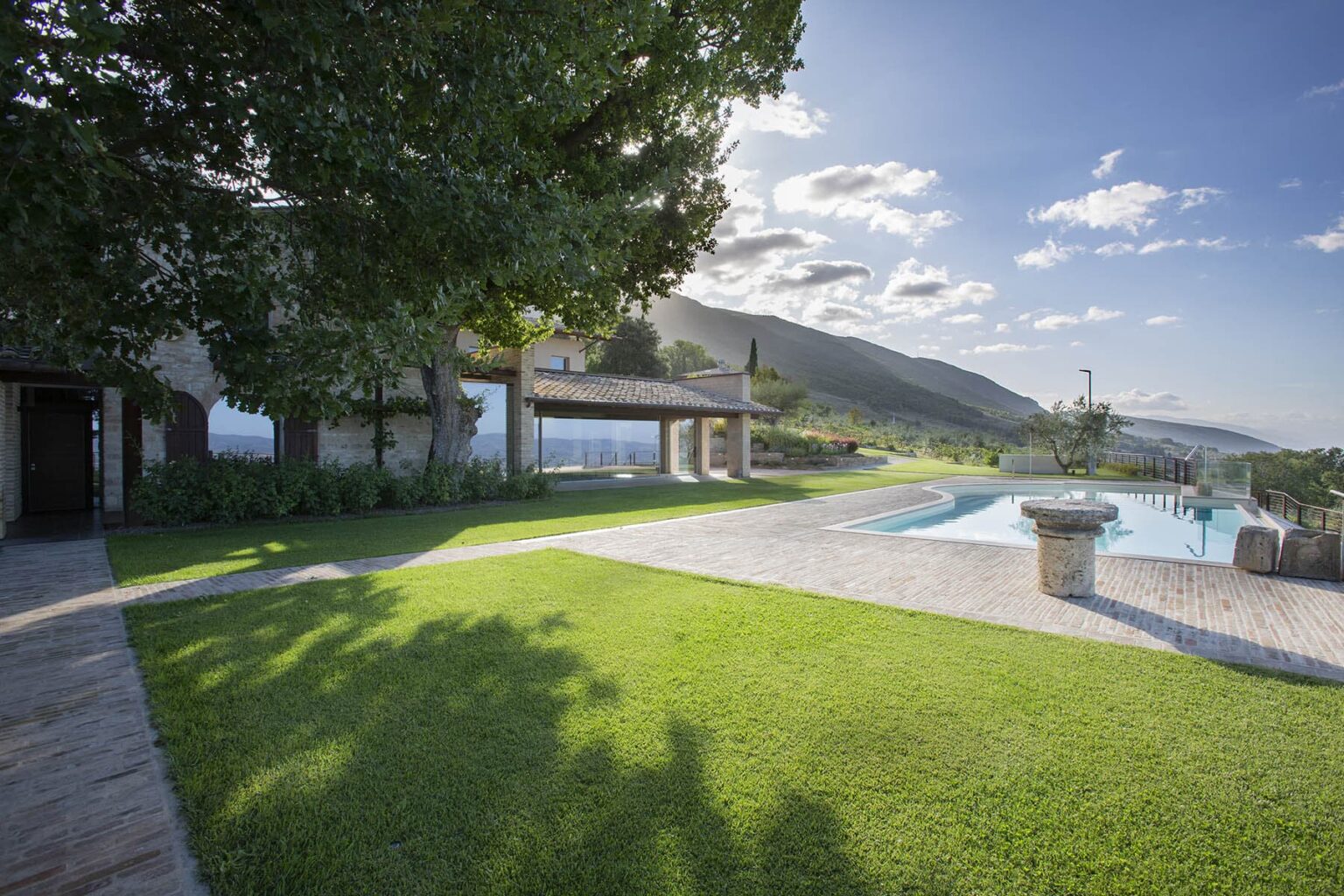 Scenic view of a landscaped garden with a swimming pool, surrounded by mountains and blue sky, highlighting a peaceful outdoor retreat. | Only on SopranoVillas