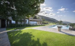 Scenic view of a landscaped garden with a swimming pool, surrounded by mountains and blue sky, highlighting a peaceful outdoor retreat.