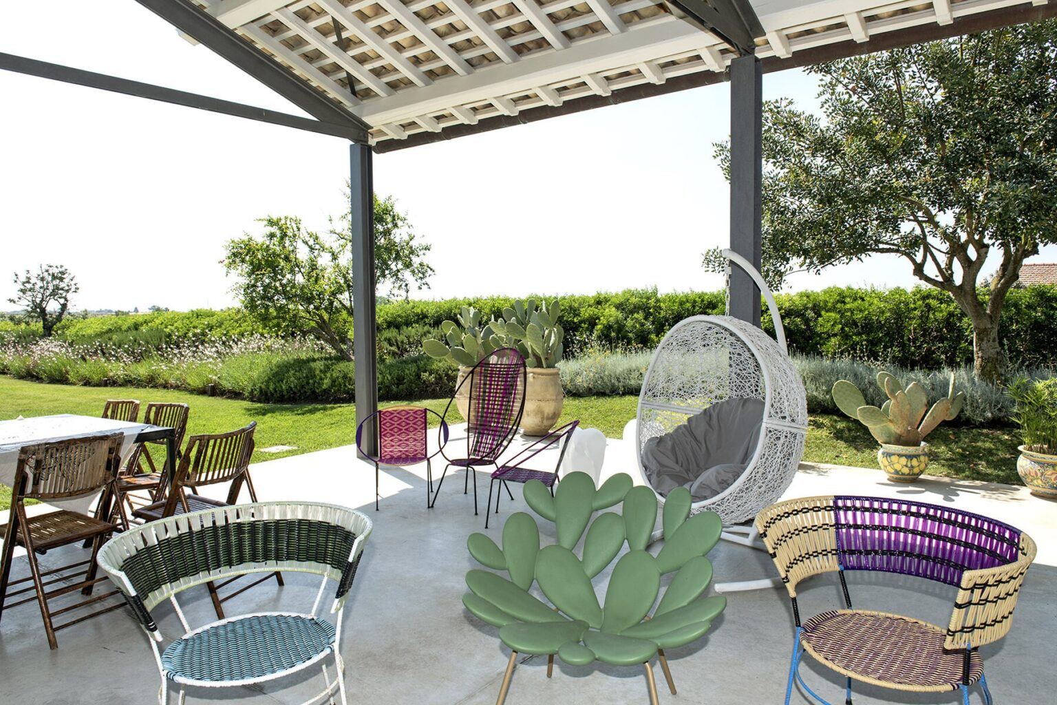 Outdoor patio featuring colorful wicker chairs and a hanging chair, surrounded by lush greenery and a serene landscape, ideal for relaxation and entertaining. | Only on SopranoVillas