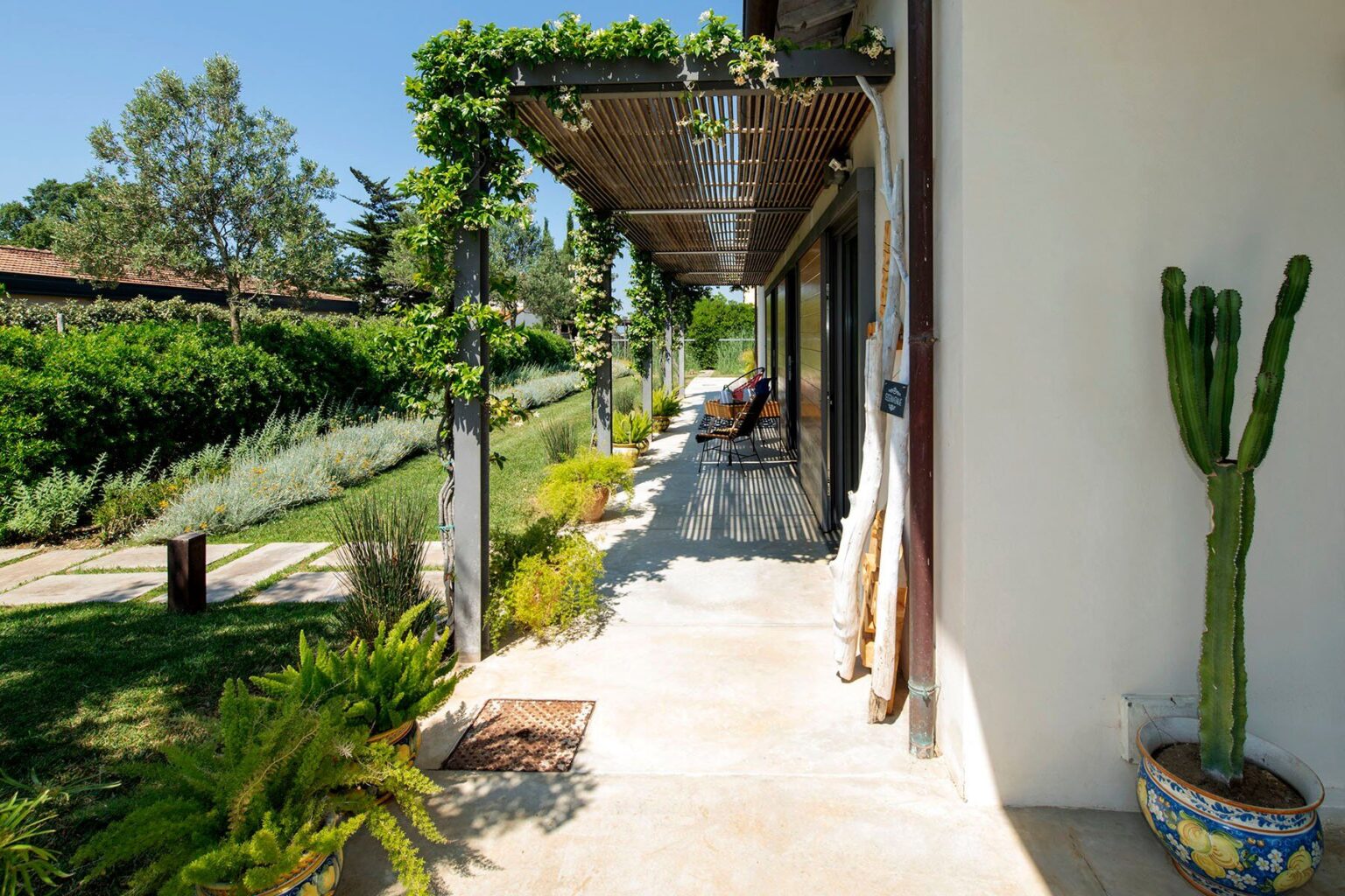Modern outdoor patio with lush greenery, featuring a cactus and a shaded walkway, ideal for relaxation and enjoying nature. | Only on SopranoVillas