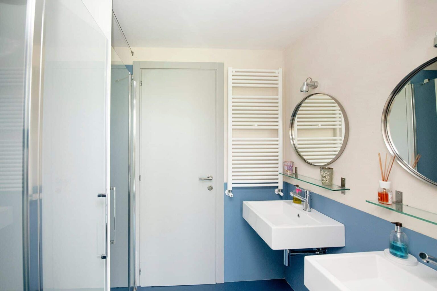 Modern bathroom interior featuring a sleek shower, minimalist sink, round mirror, and a combination of soft pink and blue walls, designed for contemporary aesthetics and functionality. | Only on SopranoVillas