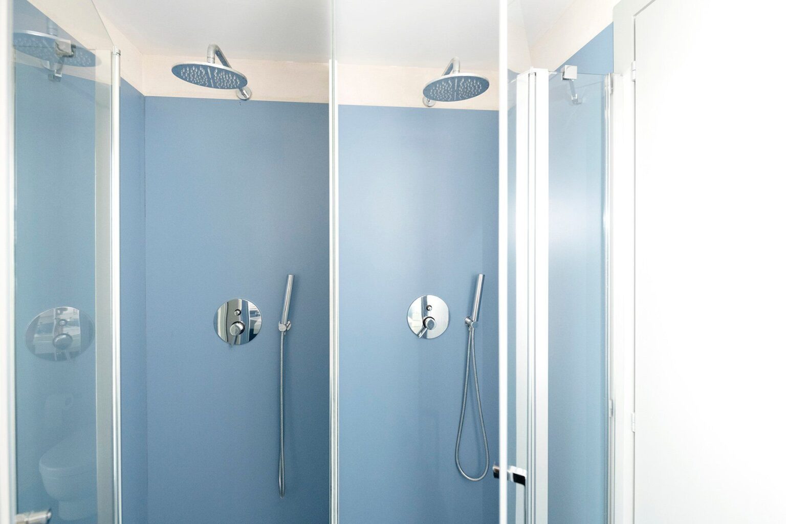 Modern shower room featuring three glass-enclosed shower stalls with chrome fixtures and a soothing blue wall color, designed for a contemporary bathroom aesthetic. | Only on SopranoVillas