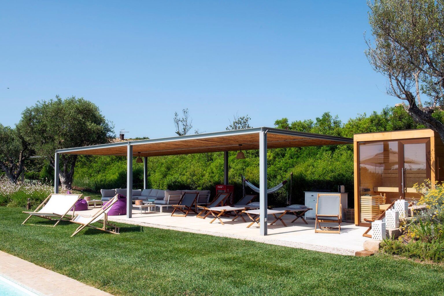 Modern outdoor lounge area featuring a shaded pergola, comfortable seating, and lush greenery, ideal for relaxation and social gatherings. | Only on SopranoVillas