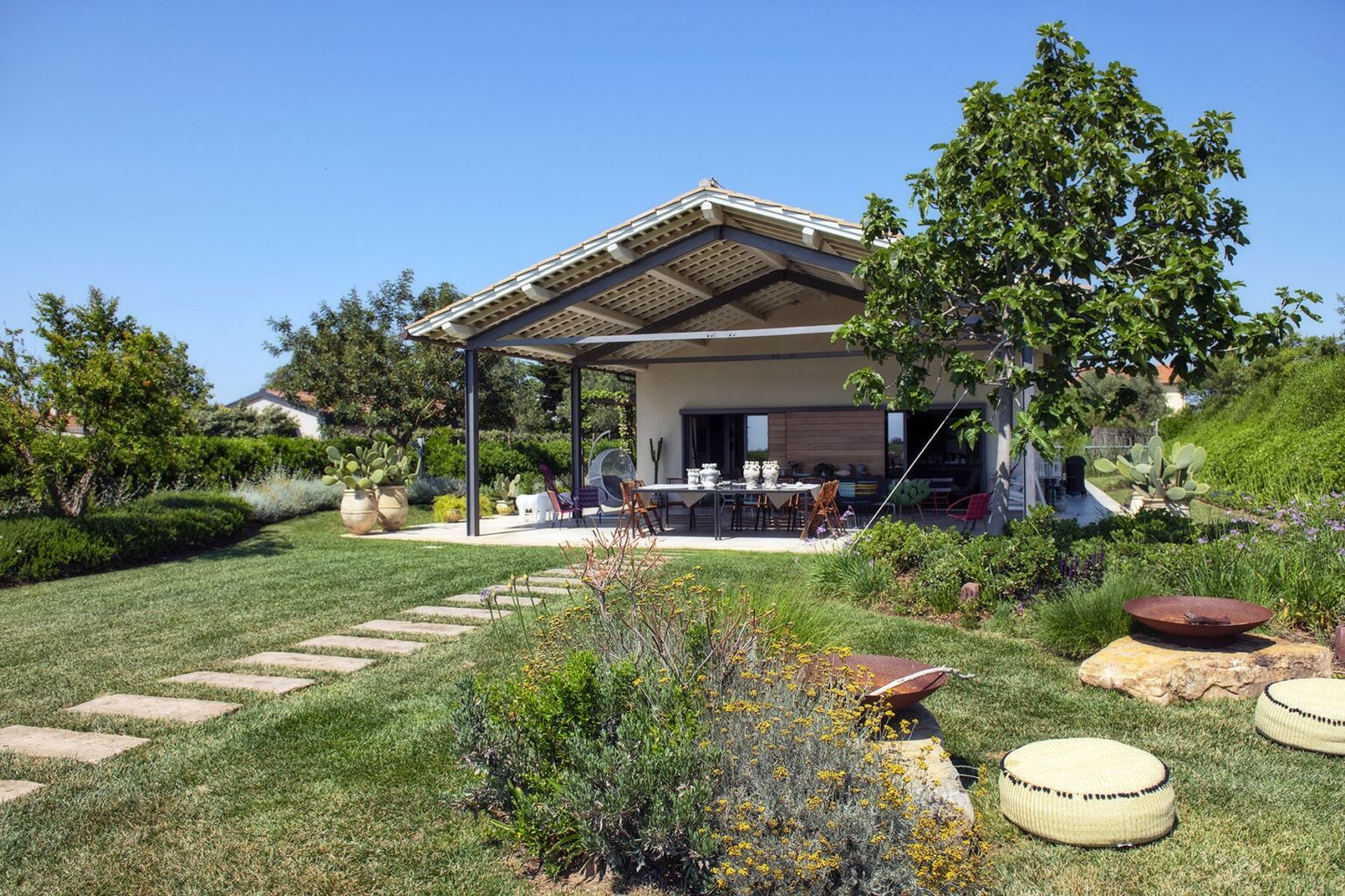 Modern outdoor patio with a covered seating area, surrounded by lush greenery and landscaped gardens, featuring stone pathways and decorative elements. Ideal for relaxation and entertaining. | Only on SopranoVillas