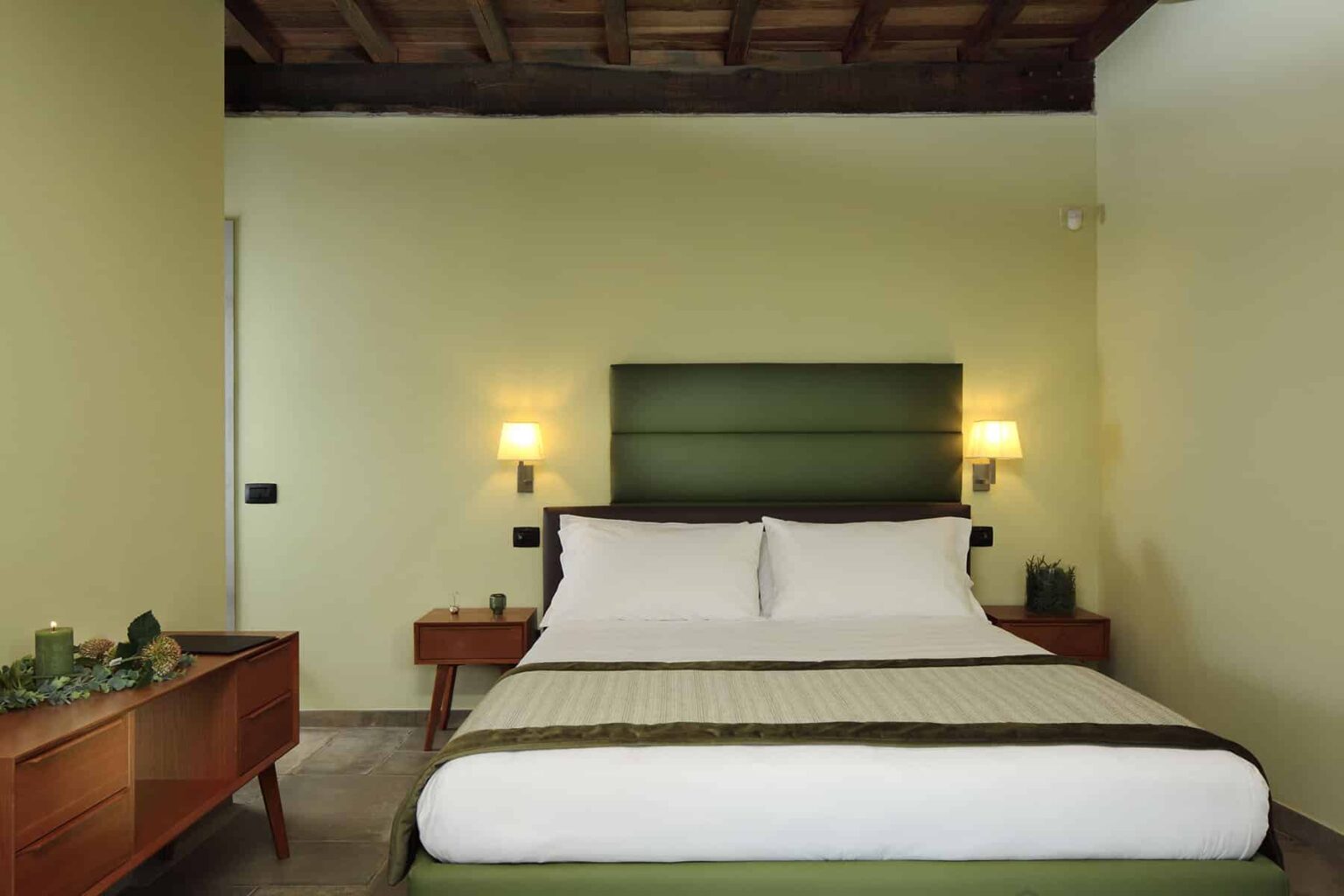 Cozy bedroom featuring a comfortable double bed with white linens, green headboard, and stylish wooden furniture, complemented by soft lighting and a warm color palette. Ideal for relaxation and comfort. | Only on SopranoVillas