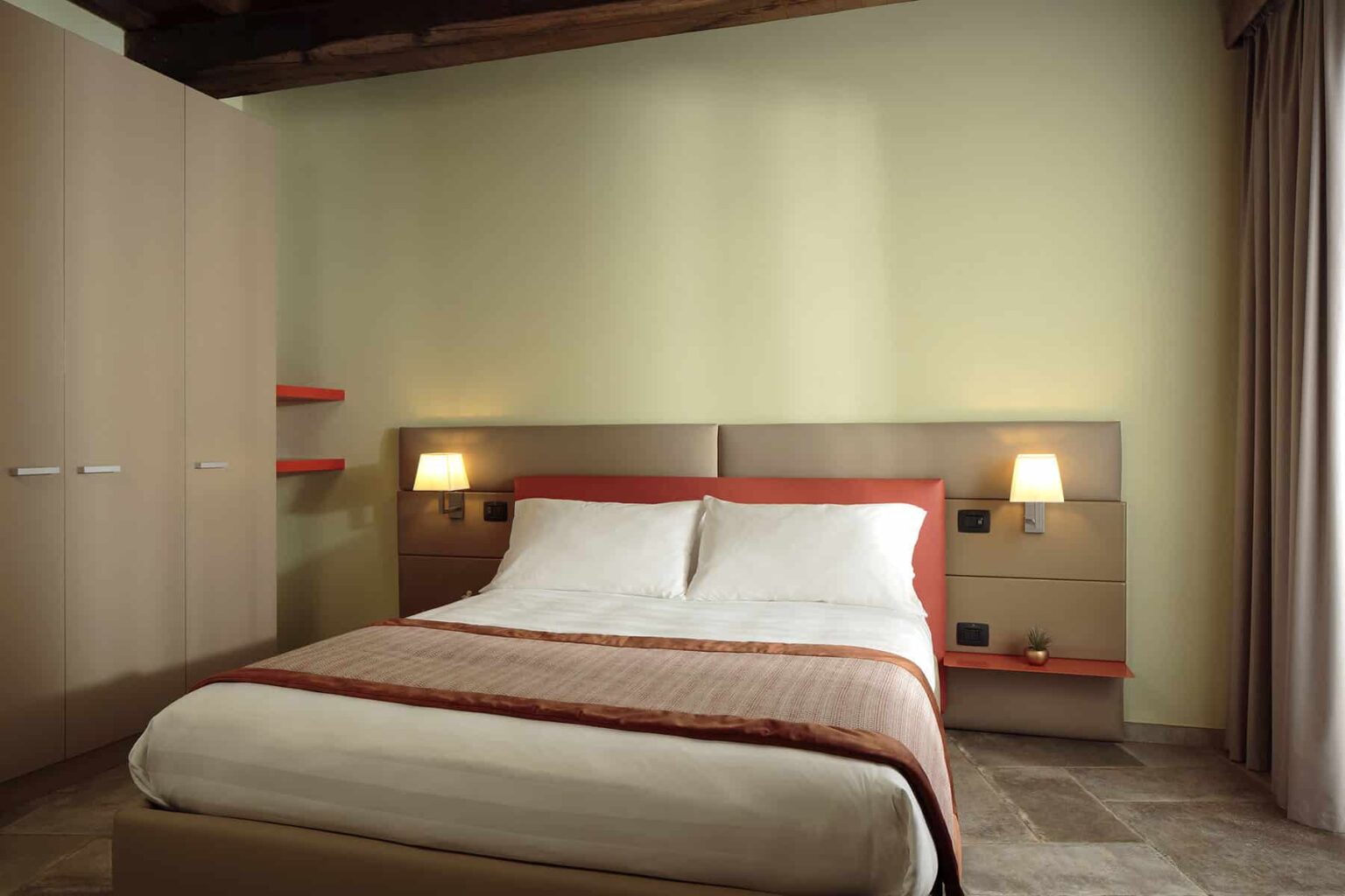 Modern bedroom interior featuring a comfortable double bed with white linens, stylish bedside lamps, and minimalistic furniture against a light green wall. Ideal for relaxation and restful stays. | Only on SopranoVillas