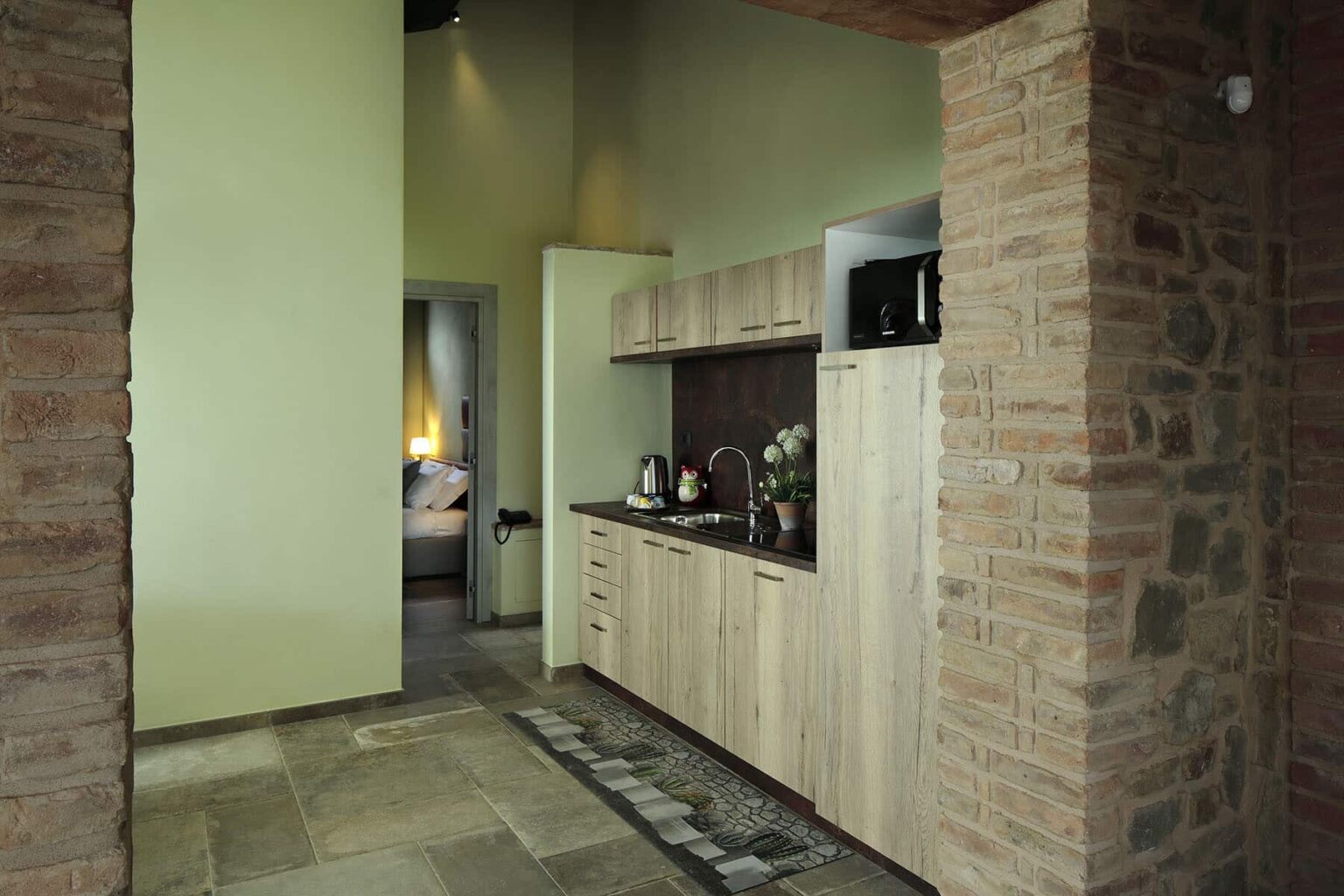 Modern kitchen interior featuring wooden cabinetry, stone walls, and a cozy atmosphere. The design includes a sleek countertop, essential kitchen appliances, and a warm color palette, creating a welcoming space. | Only on SopranoVillas