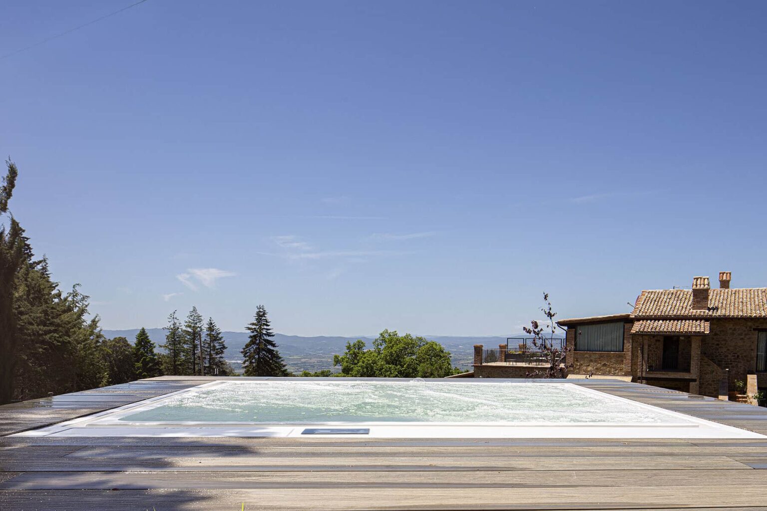 Luxury infinity pool overlooking a scenic landscape with a clear blue sky and a rustic home nearby. Ideal for relaxation and outdoor living. | Only on SopranoVillas