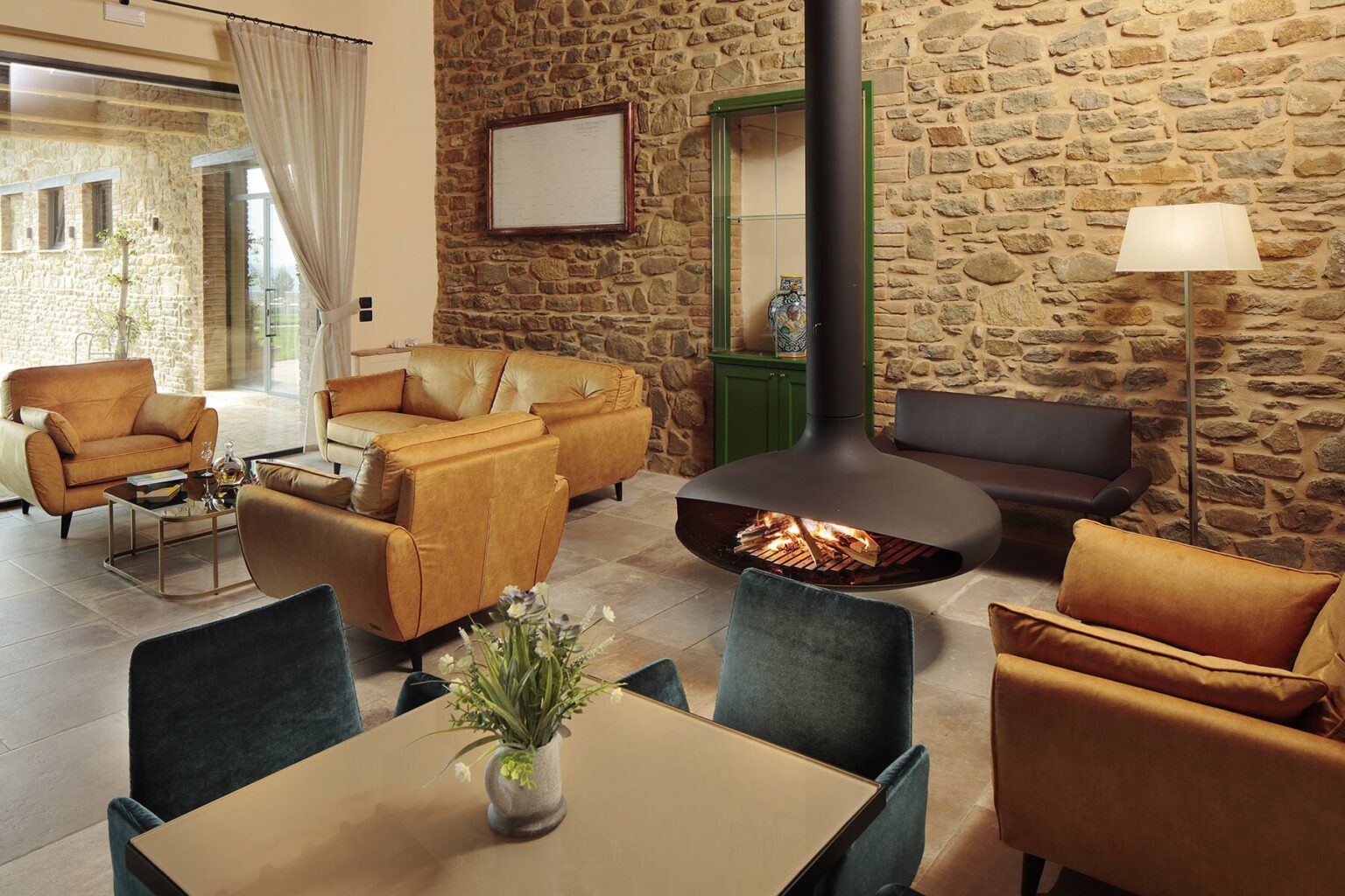 Cozy living room featuring a stone wall, comfortable seating with orange and teal sofas, a modern coffee table with a vase of flowers, and a stylish fireplace as a focal point. Ideal for relaxation and social gatherings. | Only on SopranoVillas