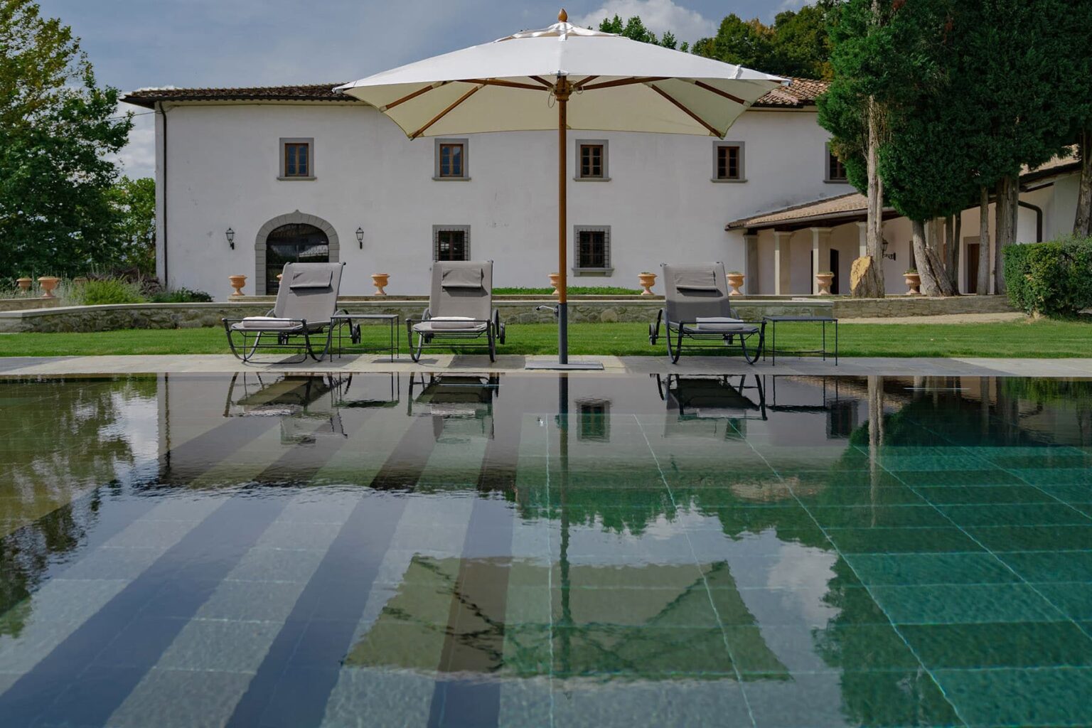 Luxury villa with a swimming pool, featuring lounge chairs and an umbrella, surrounded by lush greenery and a modern architectural design. | Only on SopranoVillas