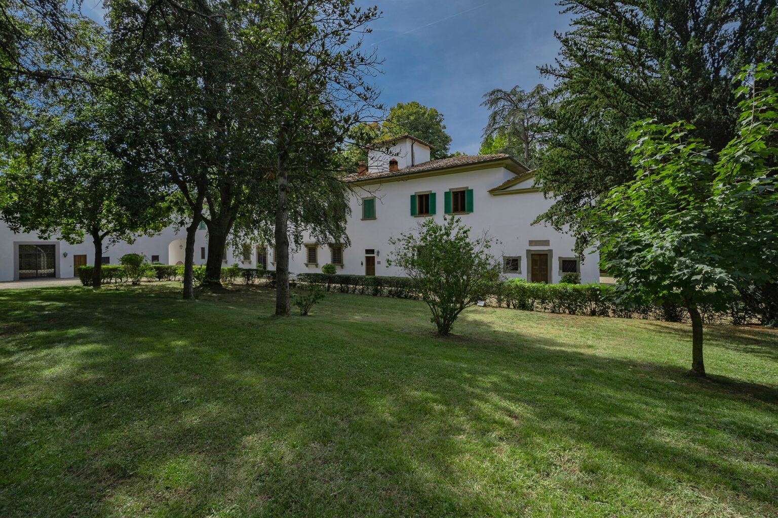 Historic white building surrounded by lush greenery and trees, set in a tranquil landscape with a cloudy sky. | Only on SopranoVillas