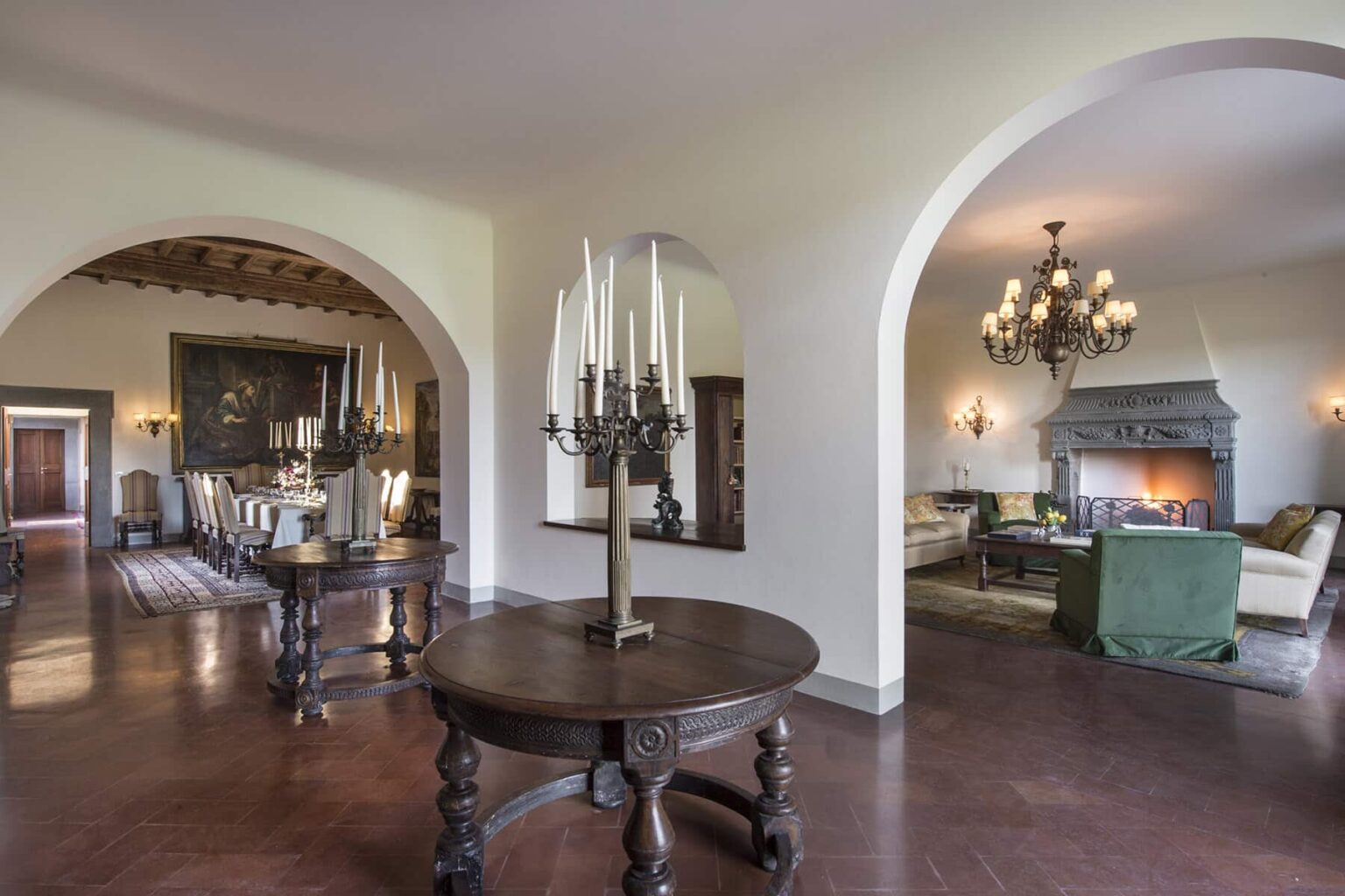 Spacious interior of a stylish living area featuring arched doorways, a decorative table with candles, elegant furniture, and a cozy fireplace, creating a warm and inviting atmosphere. | Only on SopranoVillas