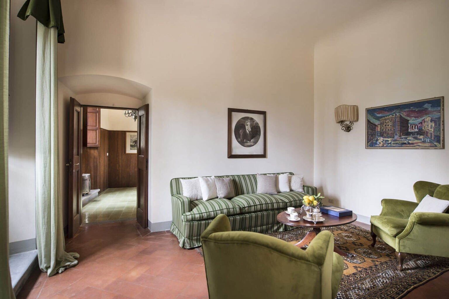 Cozy living room featuring a green striped sofa, two green armchairs, a coffee table with flowers, and artwork on the walls, illuminated by natural light from large windows. | Only on SopranoVillas