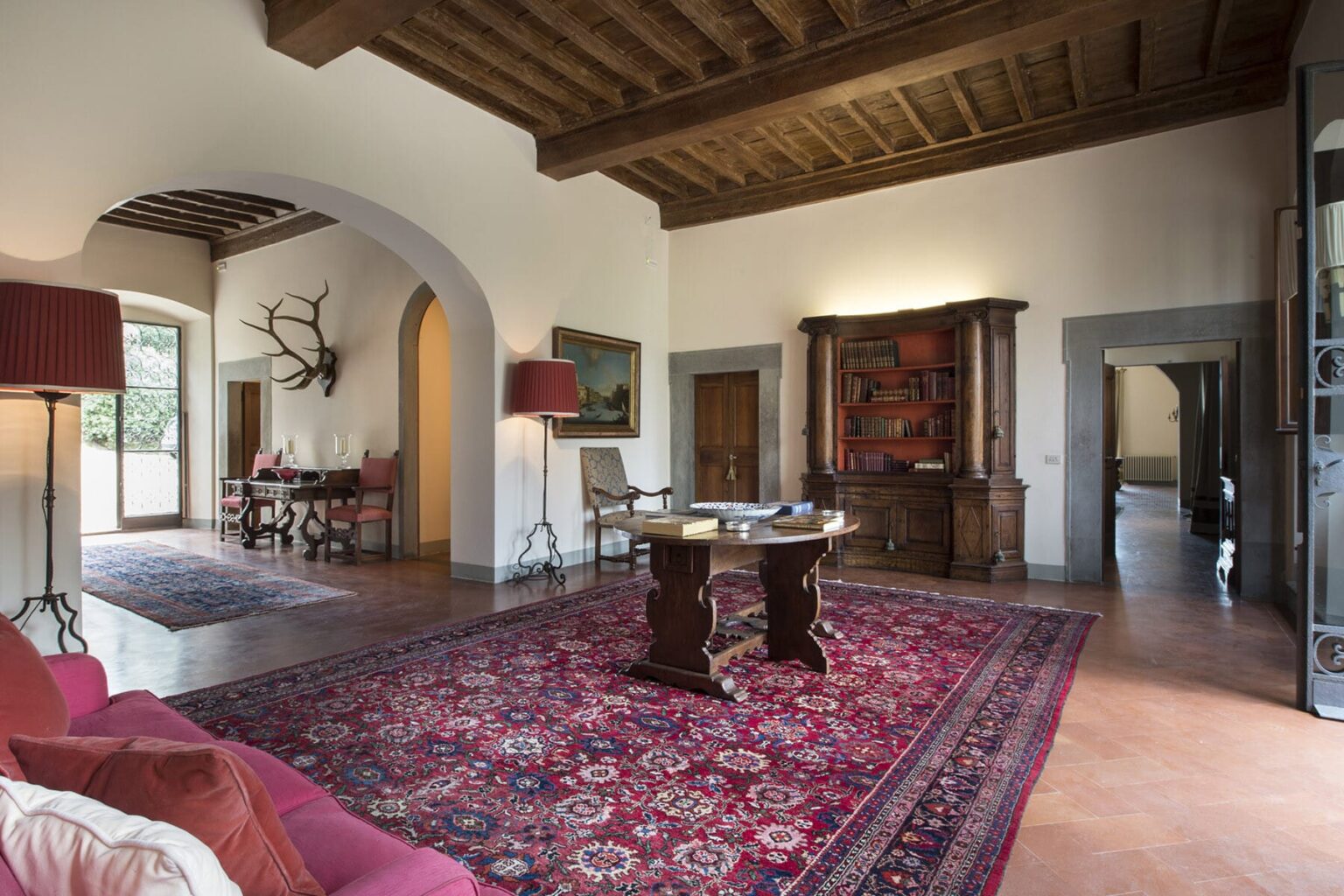Spacious living room with high wooden ceilings, elegant furnishings, and a vintage rug. The room features a decorative wooden cabinet and a cozy seating area, creating a warm and inviting atmosphere. | Only on SopranoVillas
