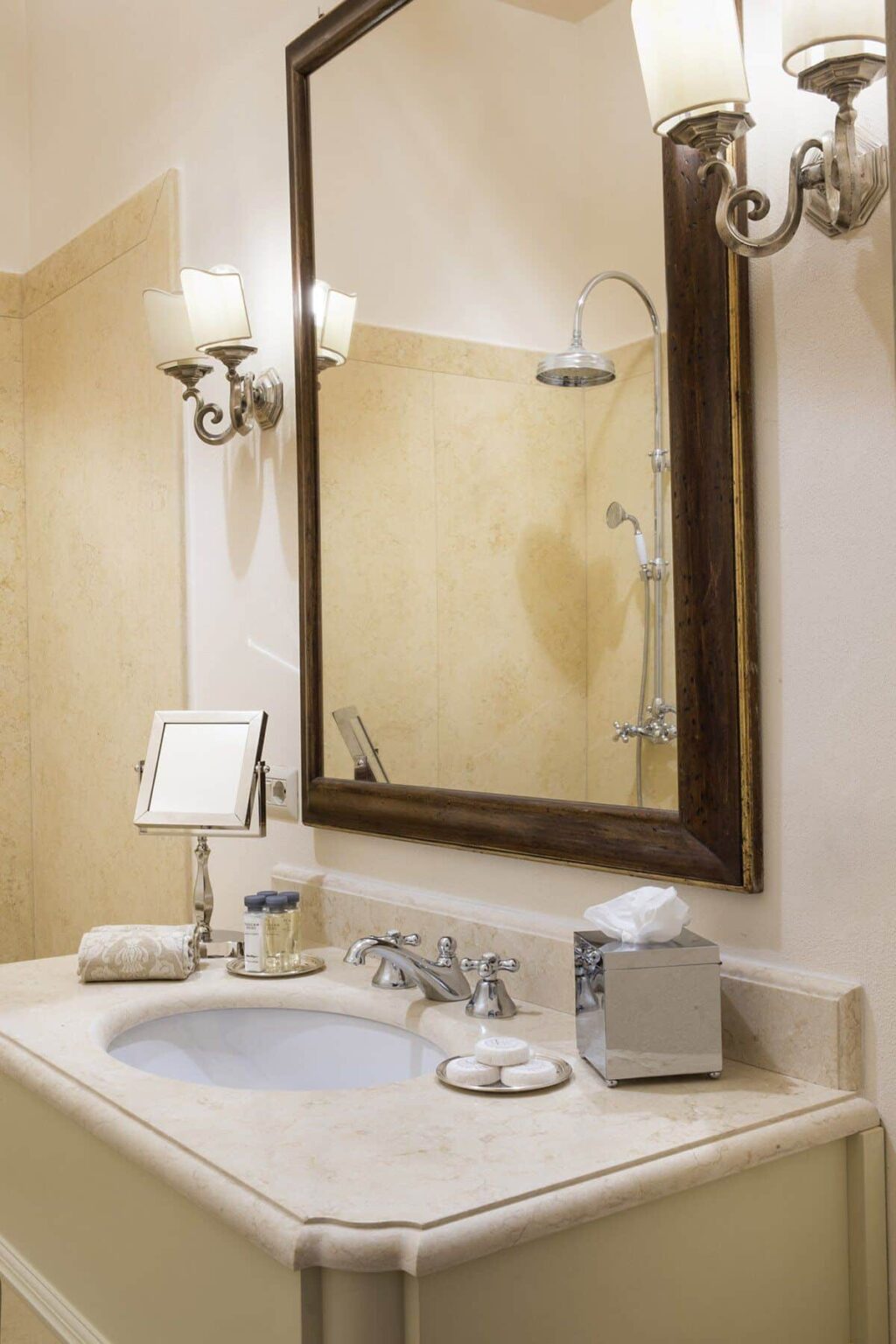 Modern bathroom interior featuring a large framed mirror, elegant wall sconce, and stylish sink area with toiletries. | Only on SopranoVillas