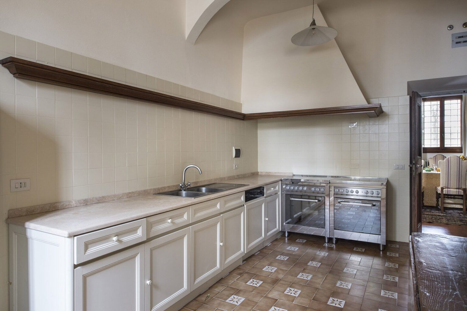 Spacious modern kitchen featuring white cabinetry, stainless steel appliances, and a large countertop, complemented by a tiled floor and natural light from nearby windows. | Only on SopranoVillas
