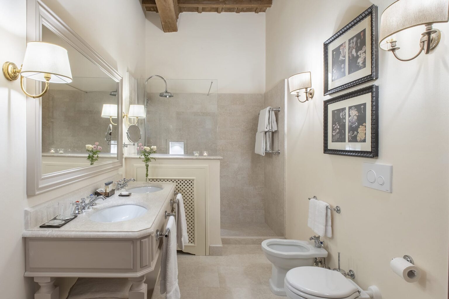 Elegant bathroom featuring a double vanity with a large mirror, stylish light fixtures, and decorative wall art. The space includes a modern toilet and towel rack, complemented by neutral tones and natural light. Ideal for home design inspiration. | Only on SopranoVillas