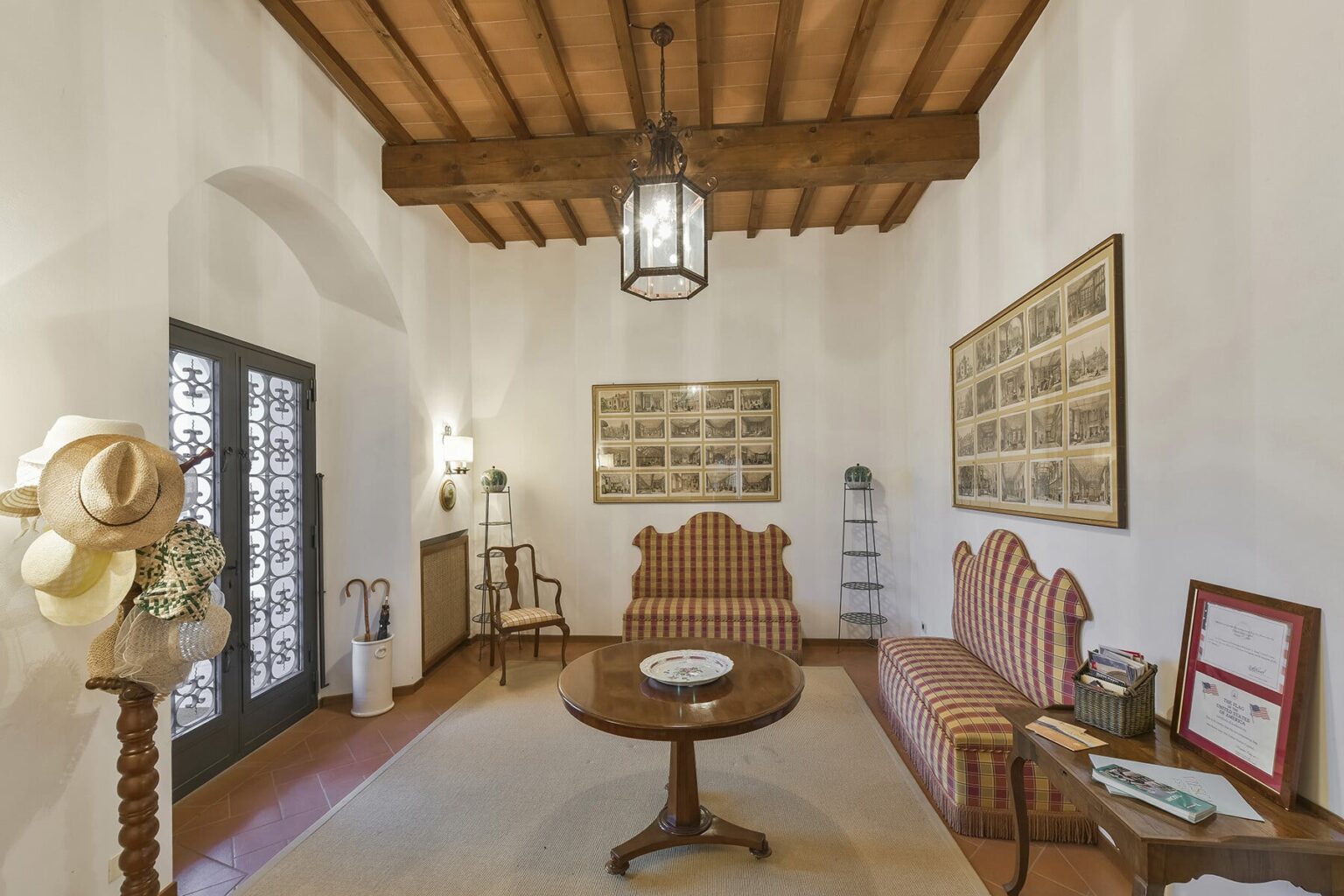 Cozy living room interior featuring a wooden beam ceiling, vintage furniture with striped upholstery, a round coffee table, and decorative wall art. The space is illuminated by a lantern-style light fixture and has a warm, inviting atmosphere. | Only on SopranoVillas