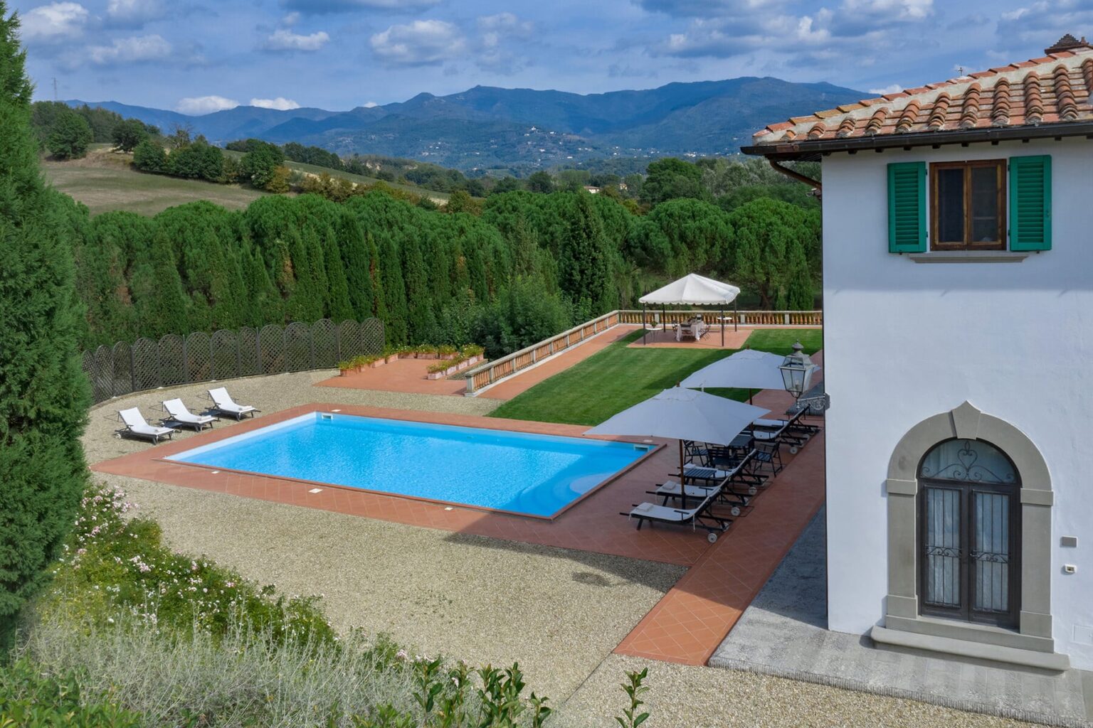 Luxury villa with a swimming pool surrounded by lush greenery and mountains in the background, featuring sun loungers and a shaded area for relaxation. Ideal for vacation rentals or getaway retreats. | Only on SopranoVillas