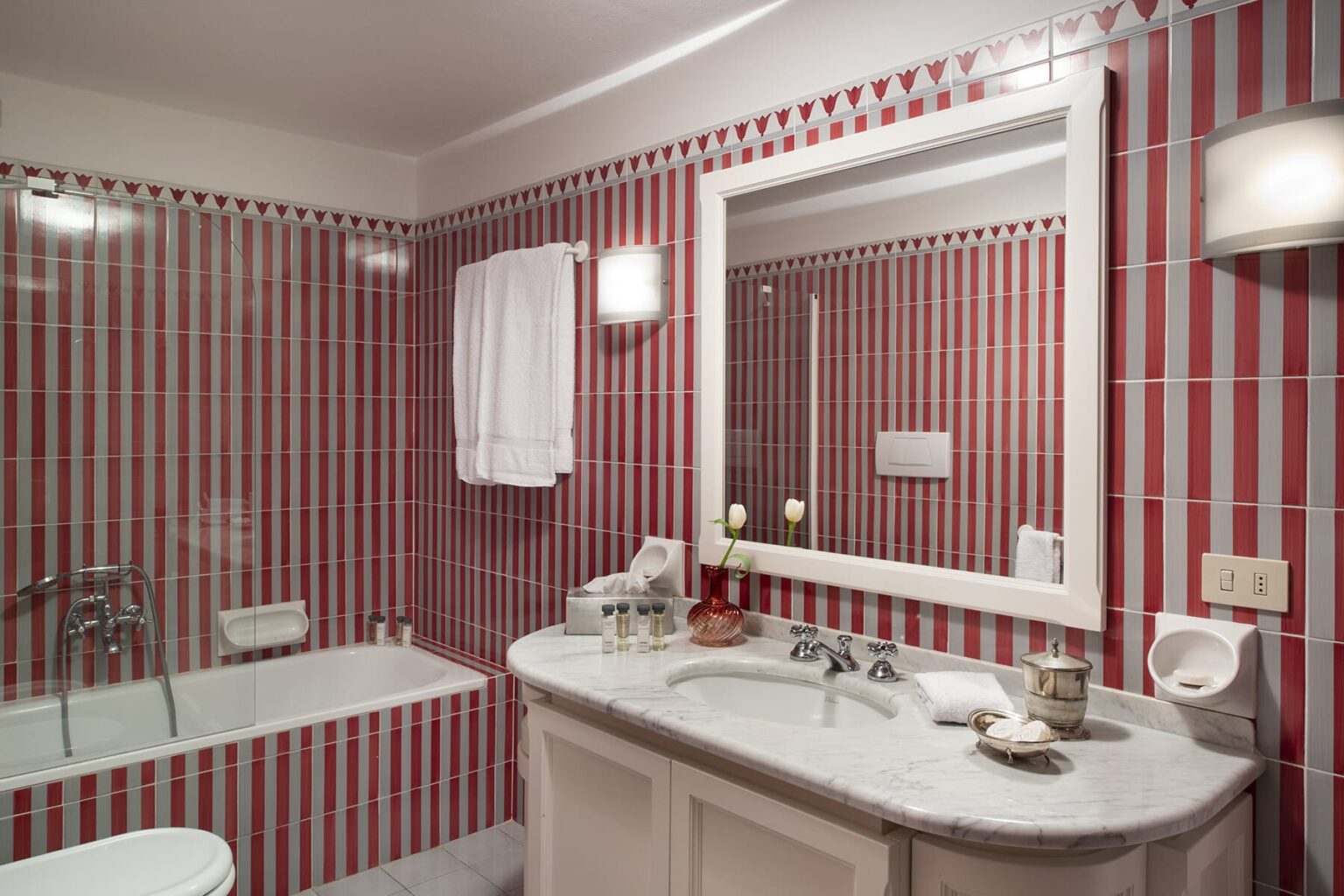 Modern bathroom featuring red striped tiles, a bathtub, a large mirror, and a vanity sink with elegant fixtures. Soft lighting enhances the contemporary design. | Only on SopranoVillas