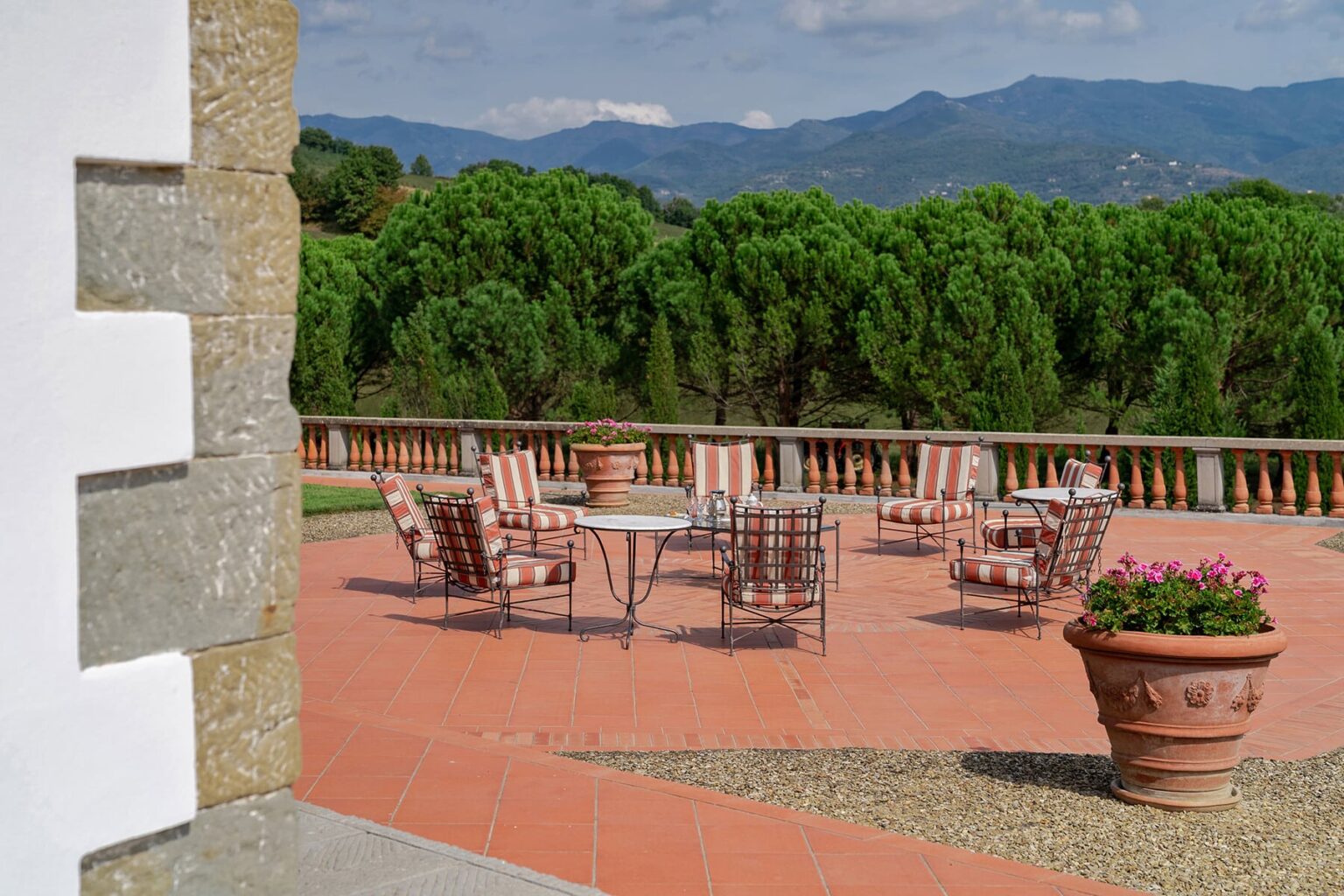 Outdoor patio with seating and mountain views in a lush landscape, featuring terracotta pots and a stone wall. Ideal for relaxation and gatherings. | Only on SopranoVillas