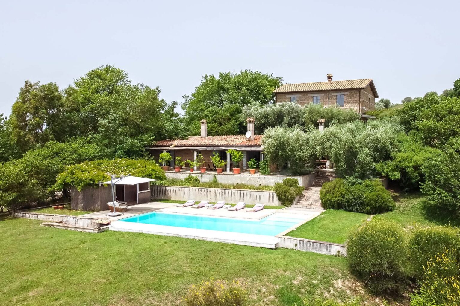 Aerial view of a luxurious villa with a swimming pool surrounded by lush greenery, featuring a spacious terrace and outdoor seating area, perfect for relaxation and entertainment. | Only on SopranoVillas