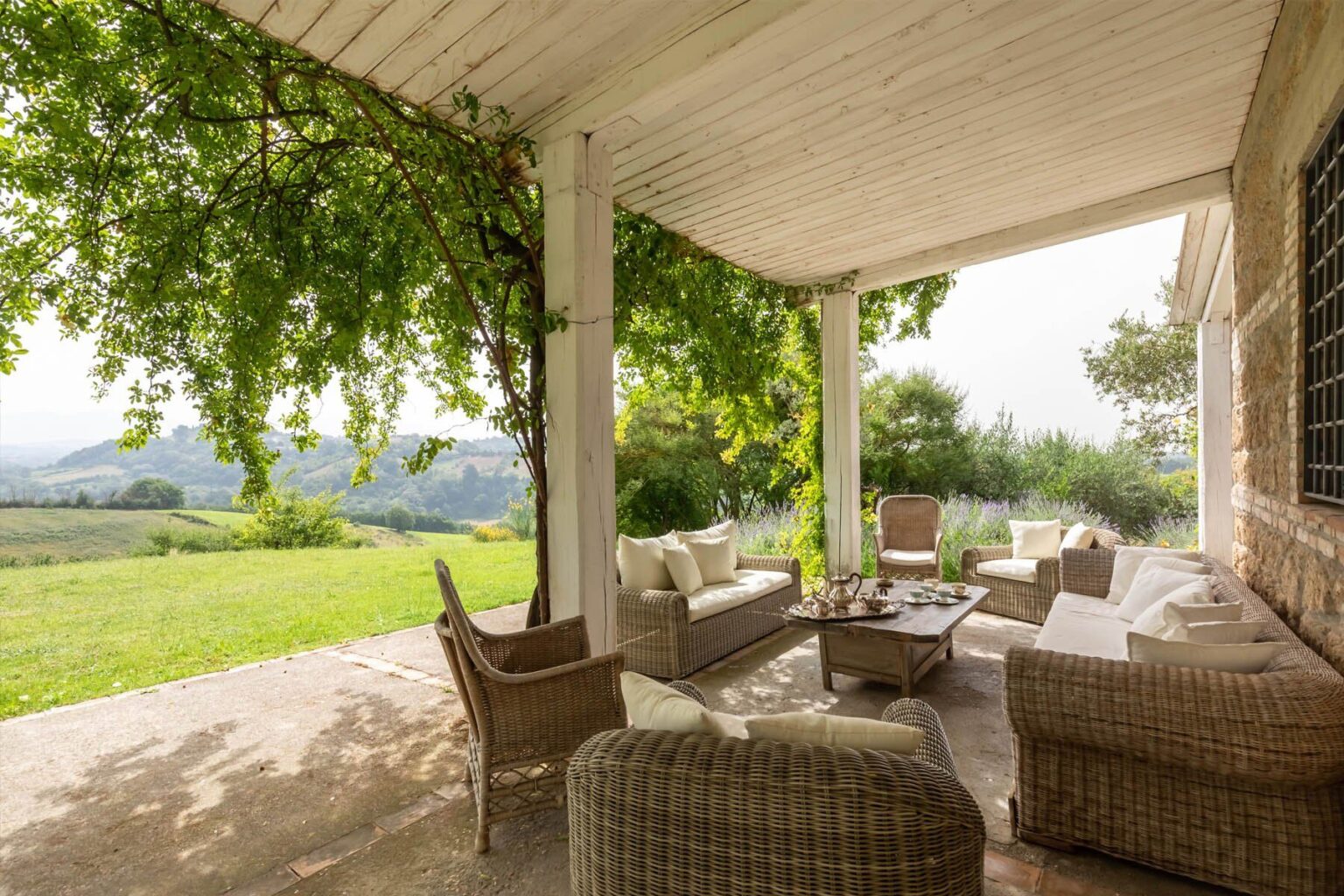 Cozy outdoor seating area with wicker furniture under a shaded porch, surrounded by lush greenery and scenic views of rolling hills. Perfect for relaxation and enjoying nature. | Only on SopranoVillas