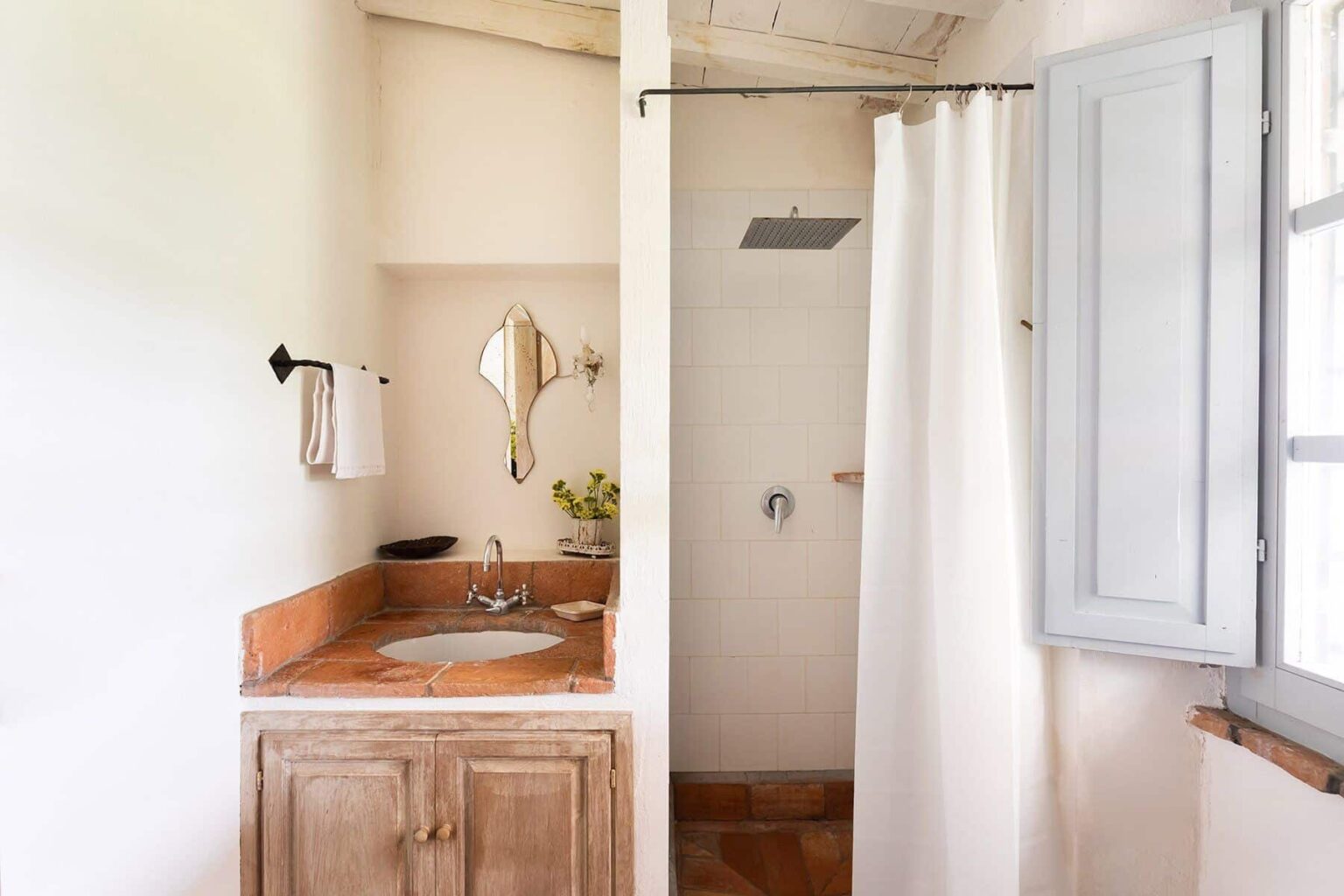 Modern bathroom design featuring a shower with a white curtain, a wooden vanity with a sink, and natural light from a window. | Only on SopranoVillas