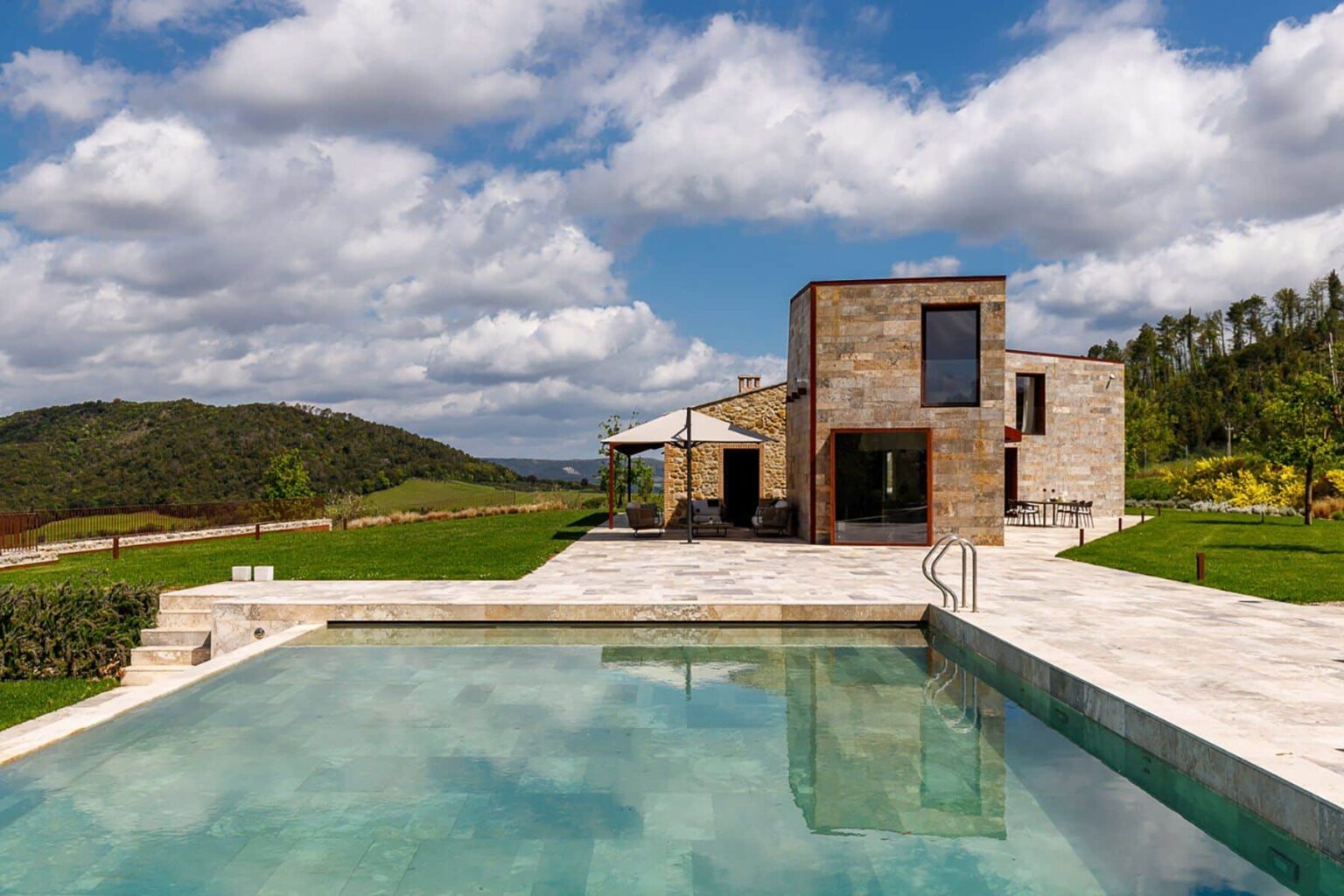 Modern luxury villa with a swimming pool, surrounded by lush greenery and rolling hills under a partly cloudy sky. Ideal for relaxation and outdoor living. | Only on SopranoVillas