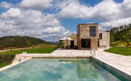 Modern luxury villa with a swimming pool, surrounded by lush greenery and rolling hills under a partly cloudy sky. Ideal for relaxation and outdoor living.