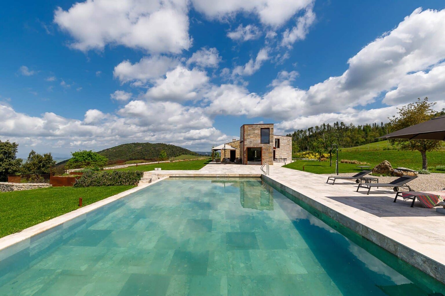 Luxury villa with a stunning infinity pool surrounded by lush green hills and a clear blue sky, ideal for relaxation and outdoor living. | Only on SopranoVillas