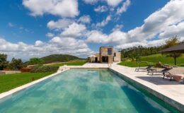 Luxury villa with a stunning infinity pool surrounded by lush green hills and a clear blue sky, ideal for relaxation and outdoor living.