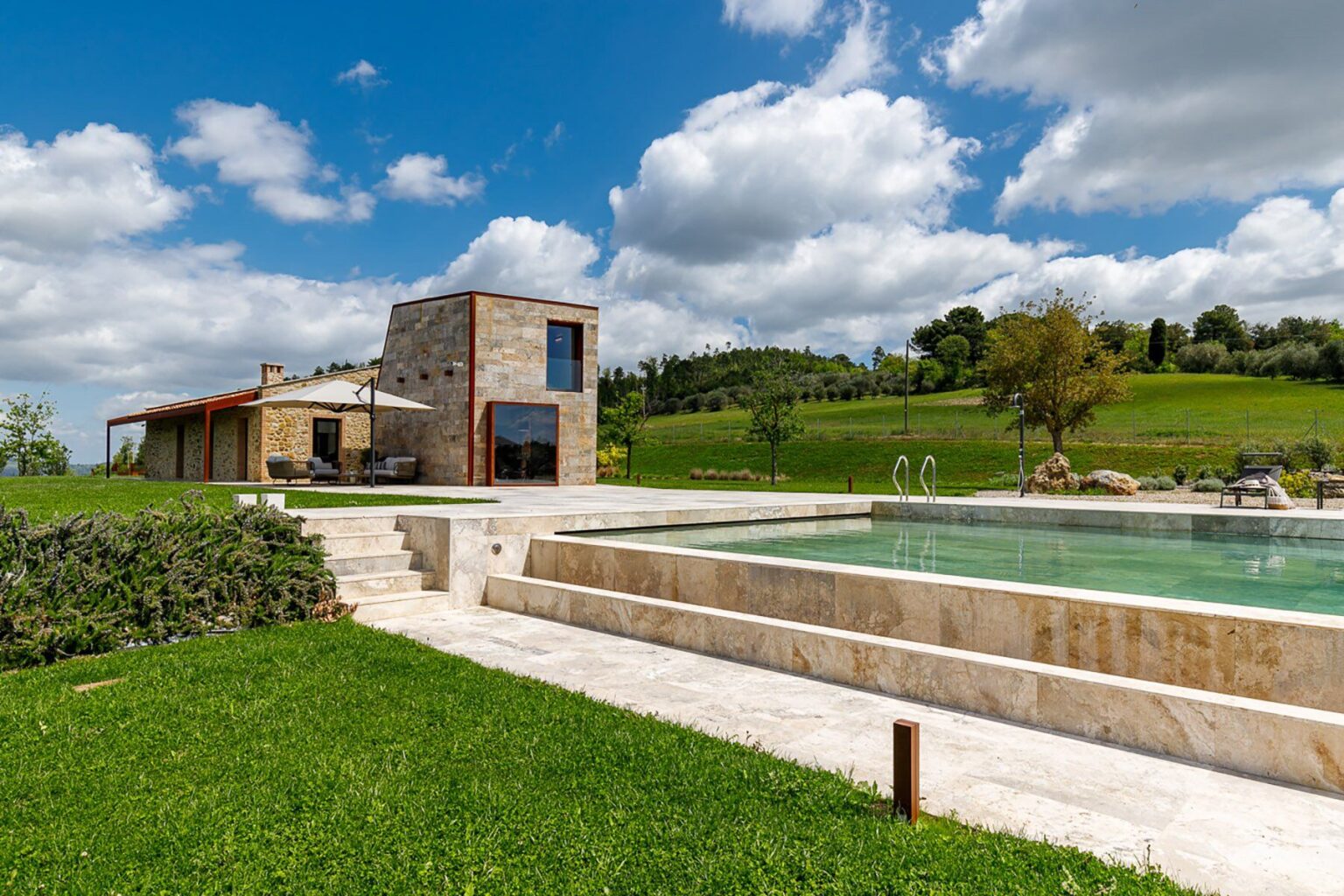 Modern stone villa with a swimming pool surrounded by lush greenery and blue skies. Ideal for luxury vacation rentals and outdoor relaxation. | Only on SopranoVillas