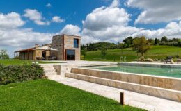 Modern stone villa with a swimming pool surrounded by lush greenery and blue skies. Ideal for luxury vacation rentals and outdoor relaxation.