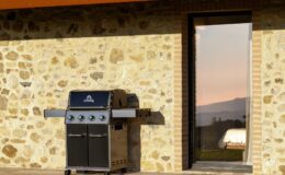 Modern gas grill on a stone patio with a large glass door, overlooking a scenic outdoor view at sunset. Perfect for outdoor cooking and entertaining.