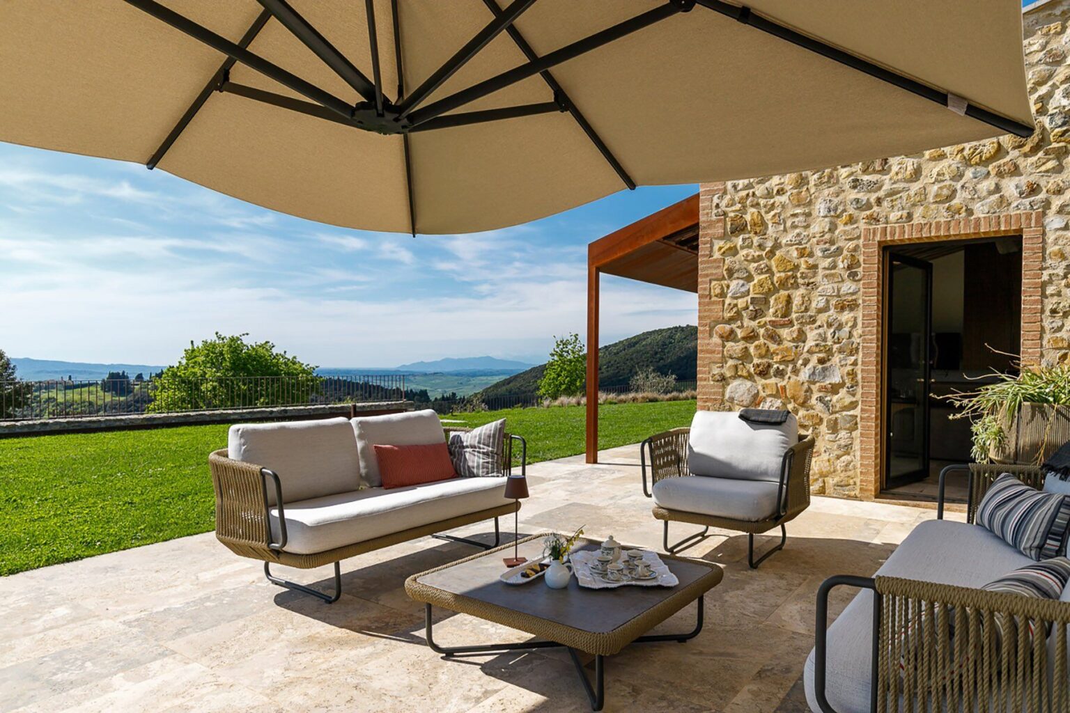 Cozy outdoor patio with stylish furniture, a large umbrella for shade, and a scenic view of hills and greenery, perfect for relaxing or entertaining. | Only on SopranoVillas