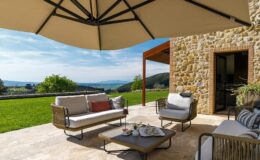 Cozy outdoor patio with stylish furniture, a large umbrella for shade, and a scenic view of hills and greenery, perfect for relaxing or entertaining.