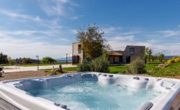 Relaxing outdoor hot tub with bubbling water, surrounded by lush greenery and a scenic view of a modern house and landscape under a clear blue sky. Perfect for leisure and wellness.