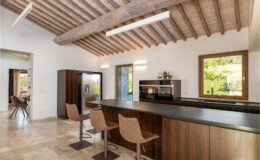 Modern kitchen interior featuring wooden beams, sleek cabinetry, and a spacious island with stylish bar stools. Natural light floods the room through large windows, enhancing the contemporary design and inviting atmosphere.