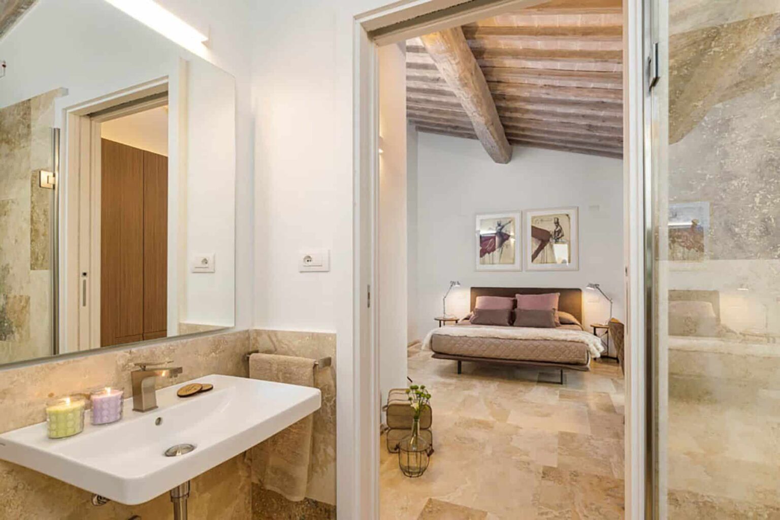 Modern bathroom with a sleek sink and natural stone accents, leading to a cozy bedroom featuring a wooden ceiling and stylish decor. Ideal for showcasing contemporary interior design and home aesthetics. | Only on SopranoVillas