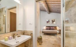 Modern bathroom with a sleek sink and natural stone accents, leading to a cozy bedroom featuring a wooden ceiling and stylish decor. Ideal for showcasing contemporary interior design and home aesthetics.