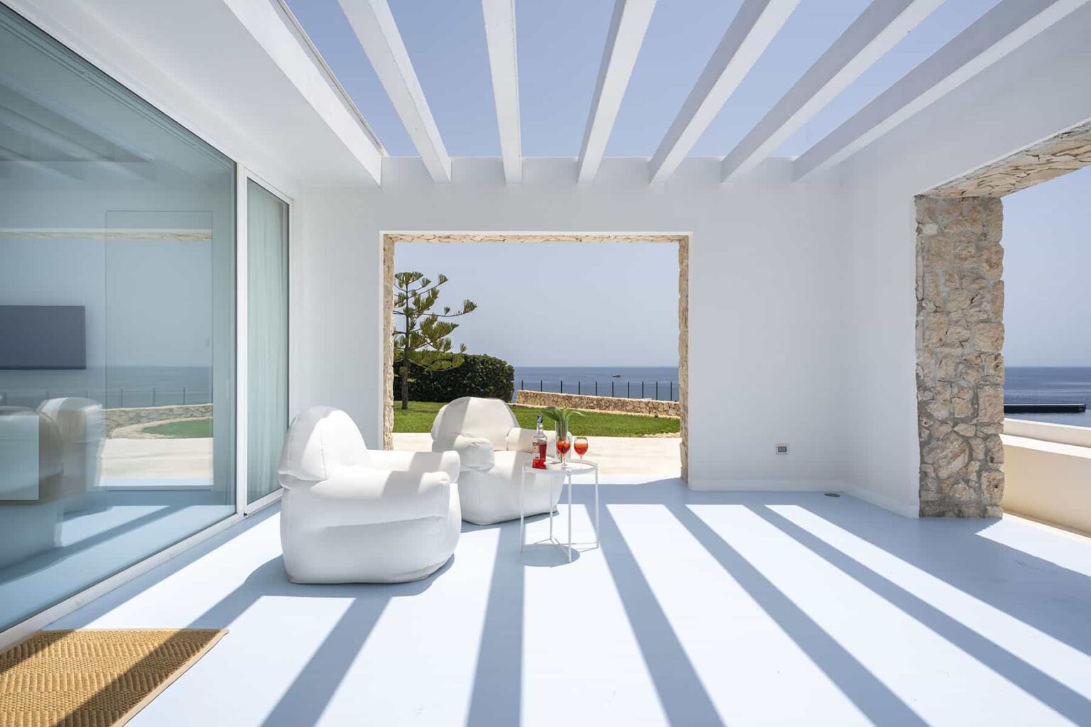 Modern coastal living room with white furniture, large glass windows, and stunning ocean views, showcasing a bright and airy atmosphere. | Only on SopranoVillas